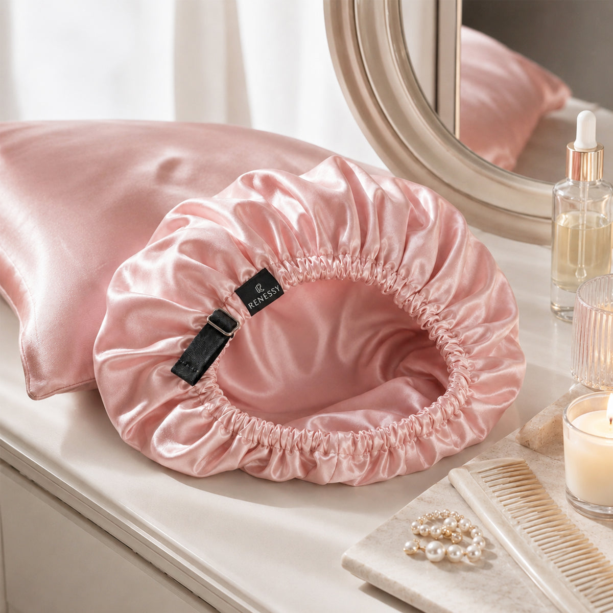 Pink Silk Bonnet lying open on a vanity next to a silk pillowcase, showing the silk lining and the adjustable strap