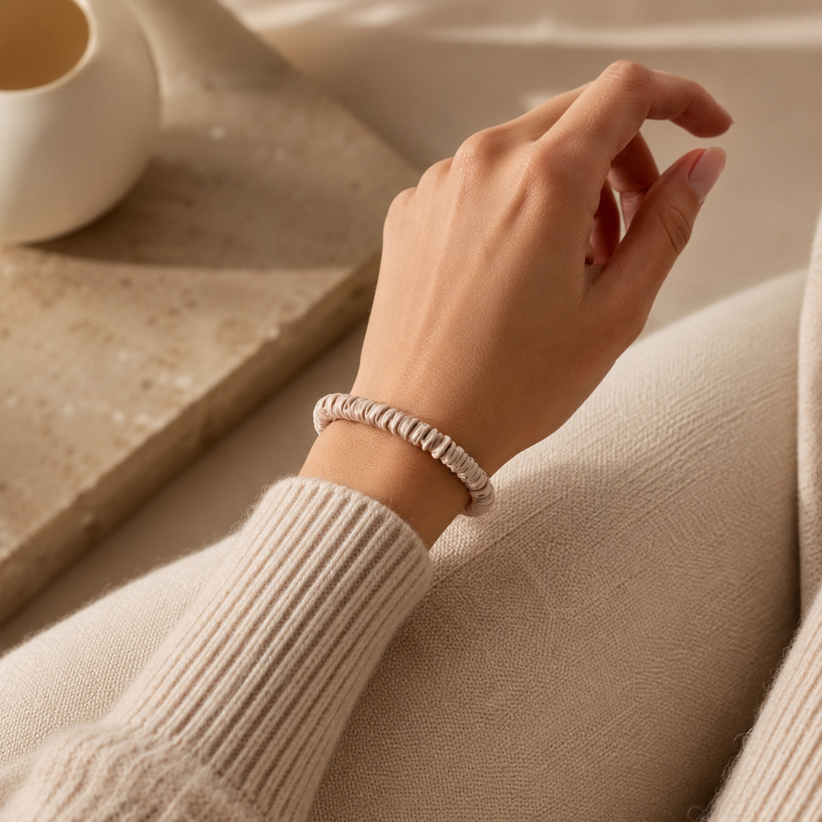 Skinny Silk Scrunchie worn on the wrist like a bracelet over a cream knit sleeve